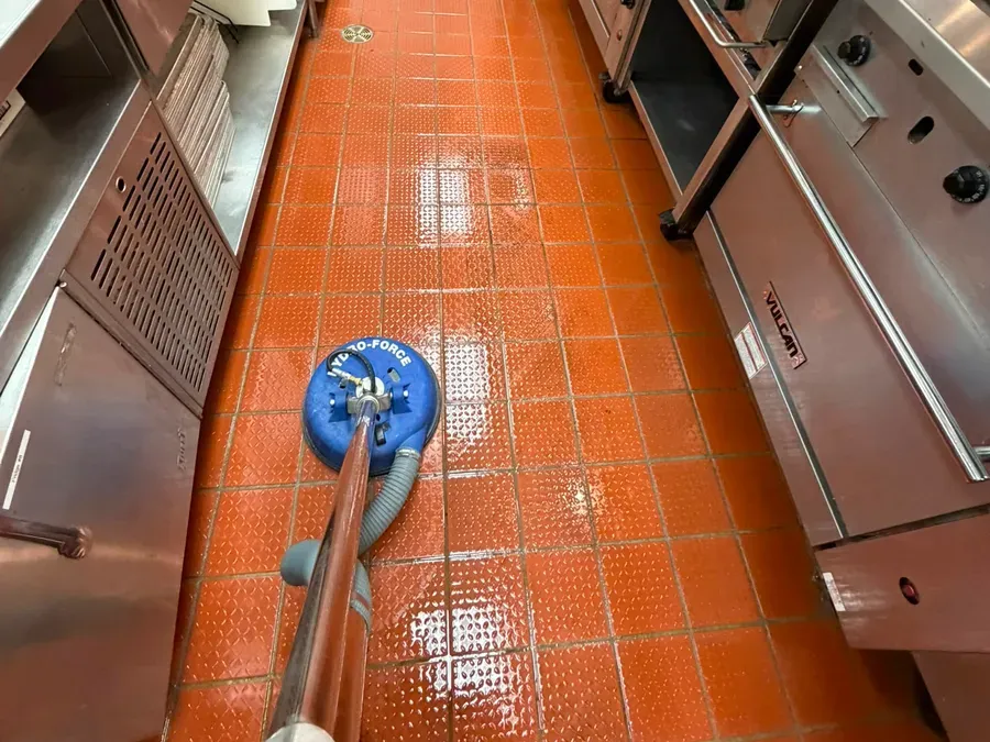 Rotary tile cleaner scrubbing the orange quarry tile floor of a commercial kitchen
