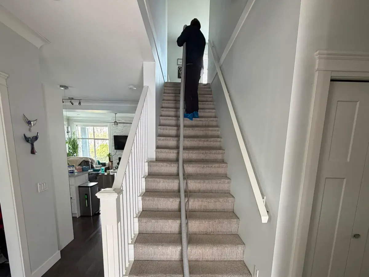Technician running an extraction wand down a full flight of carpeted stairs in a townhome