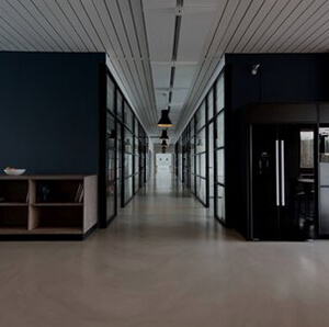 Modern office corridor with black partition walls, floor-to-ceiling glass doors, and overhead lighting.