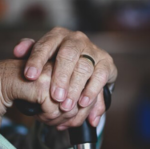 Elderly person's hands clasping a walking stick, showcasing visible signs of aging and a wedding band.