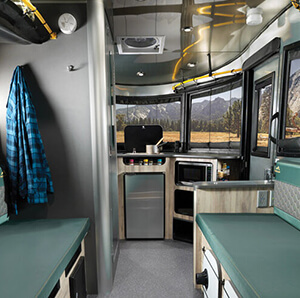 Interior of a modern camper van with kitchen amenities and seating areas, parked with a view of a mountainous landscape through its windows.