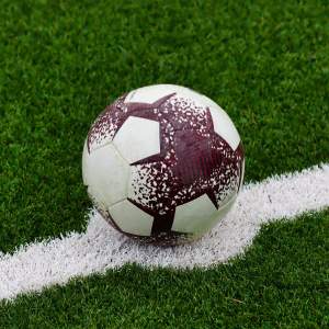 A worn soccer ball resting on the white line of a green artificial turf field.