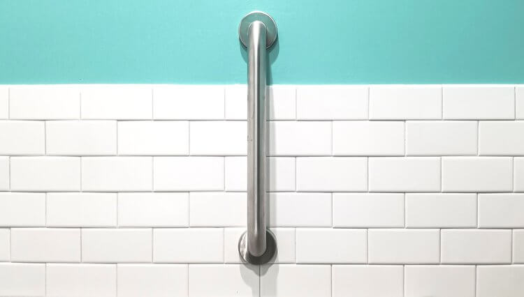 A stainless steel grab bar mounted on a white tiled wall with a turquoise background above the tiles.