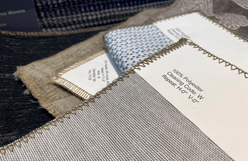 Close-up of various fabric samples, showcasing different textures and patterns. A fabric label indicating "100% Polyester" and cleaning code is visible on one sample.