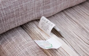 Close-up of fabric care labels on a beige textile item showing washing, drying, and ironing instructions.